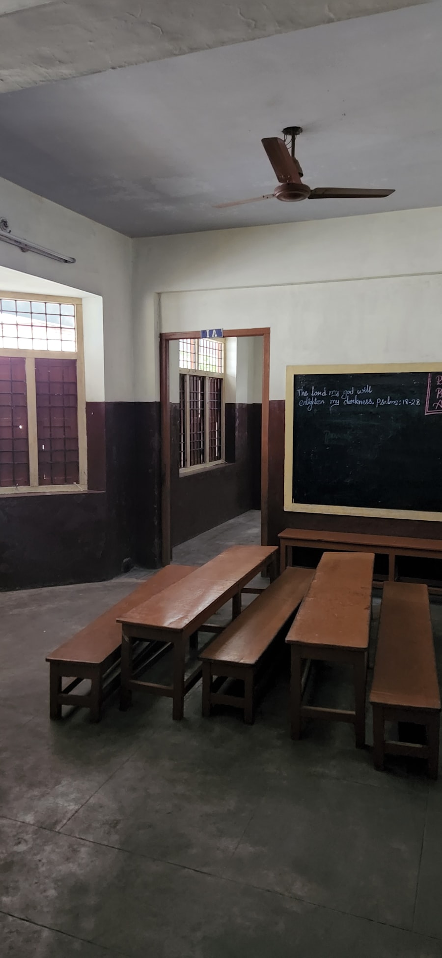 A simple classroom with wooden benches and a chalkboard.